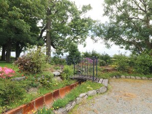 Un jardín con cerca de metal, diversas plantas y un camino de grava.