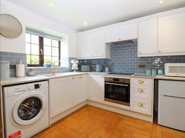 A kitchen with white cabinets, a washing machine, a microwave, and a window with blinds.