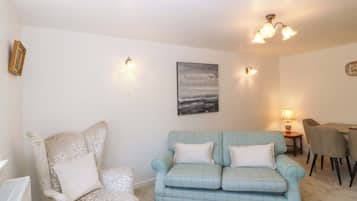 Una sala de estar con un sillón estampado, un sofá azul claro, un cuadro y un comedor con sillas y una mesa.