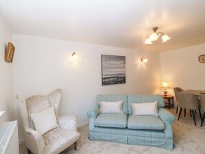 A living room with a patterned armchair, a light blue sofa, a painting, and a dining area with chairs and a table.