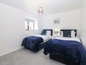 A bedroom with two beds, a window, a picture on the wall, and a hanging light fixture. - Cil Y Coed (Gaerwen)