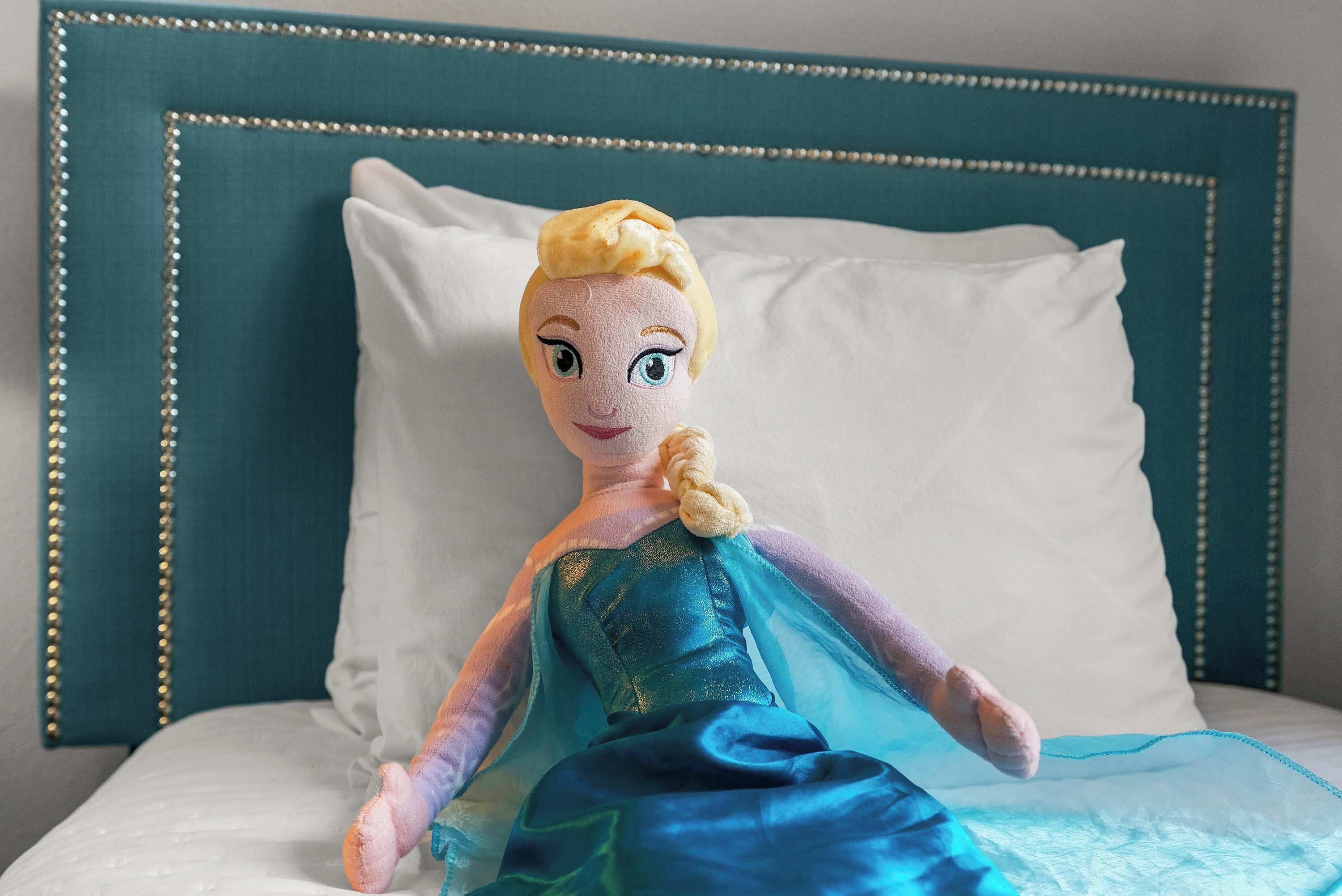 Ein Plüschtier auf einem Bett mit einem türkisnen Kopfteil und weißen Kissen.