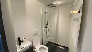 Moderni kylpyhuone, jossa on wc, suihku ja lasiseinällä varustettu suihkukaappi.