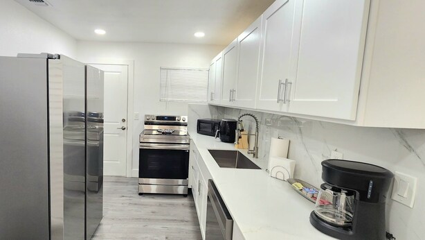 A modern kitchen with stainless steel appliances, white cabinetry, and a marble backsplash. - 2-bedroom house in fantastic Hudson with cool AC breeze (Hudson)