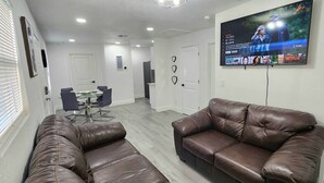 A living room with a brown leather sofa, a TV mounted on the wall, and a dining area in the background. - 2-bedroom house in fantastic Hudson with cool AC breeze (Hudson)