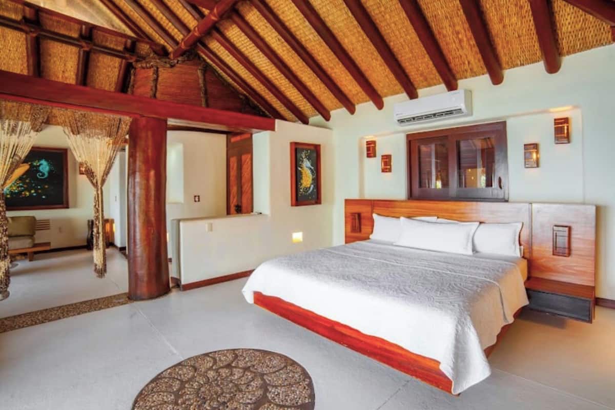 Une chambre à coucher avec un grand lit, une tête de lit en bois et un plafond recouvert de chaume.