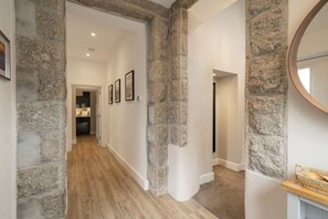 A hallway with stone walls, wooden flooring, and a kitchen visible in the background. - The Jailhouse, Historic Flat in Central Newquay (Newquay)