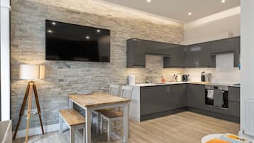 A modern kitchen with a stone wall, a flat-screen TV, and a dining area with a wooden table and chairs.