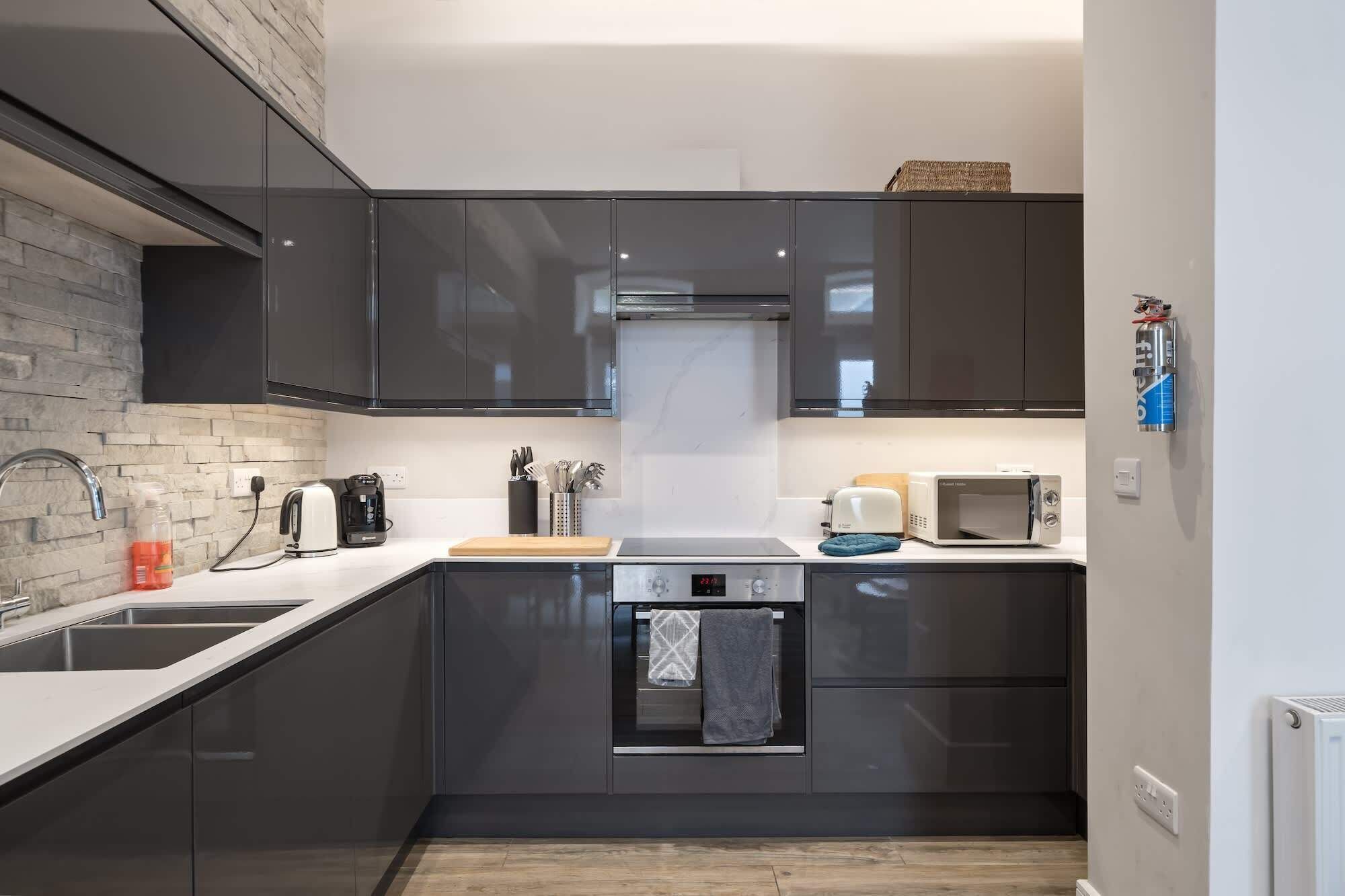 A modern kitchen with dark cabinets, a built-in oven, a microwave, and a coffee maker.