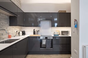 A modern kitchen with dark cabinets, a built-in oven, a microwave, and a coffee maker. - The Jailhouse, Historic Flat in Central Newquay (Newquay)