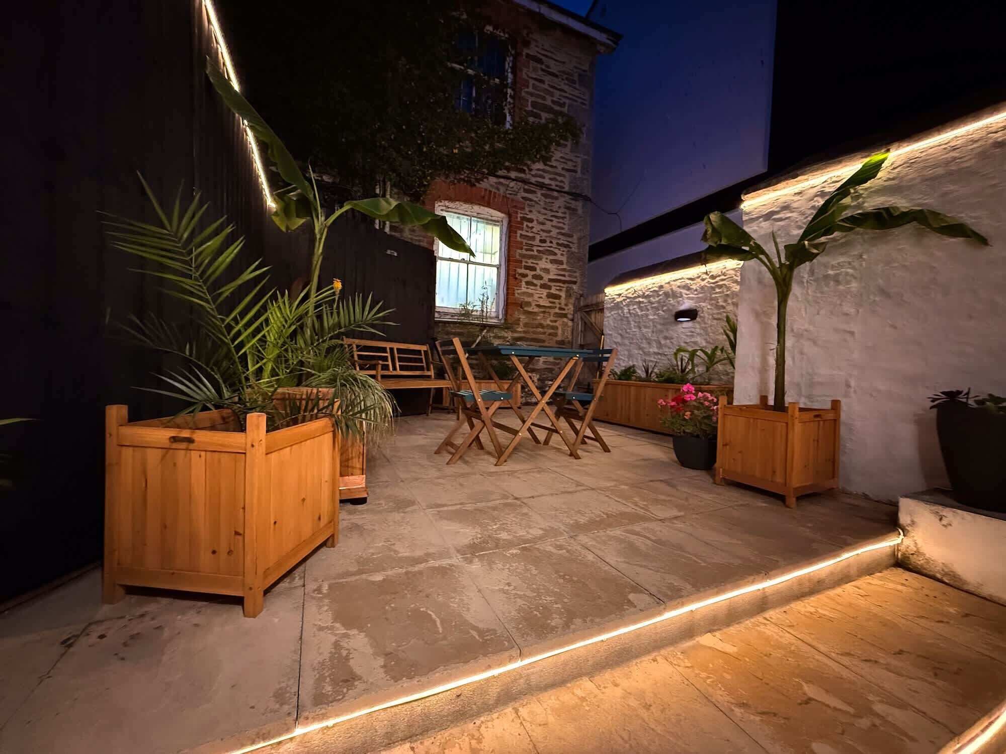 An outdoor patio with wooden furniture, potted plants, and a stone wall.