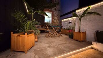 An outdoor patio with wooden furniture, potted plants, and a stone wall.
