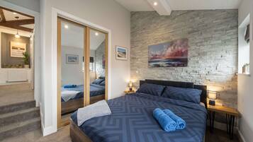 A bedroom with a large bed, a stone wall, a painting, and a view into another room.