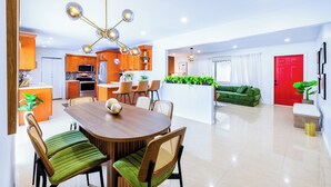 Una cocina moderna con comedor, una sala de estar con sofá verde y una puerta roja.