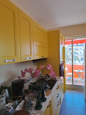 Eine Küche mit gelben Schränken, einer Arbeitsfläche mit verschiedenen Küchenutensilien und Blick auf den Balkon.