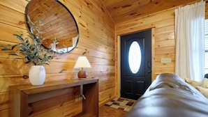 A wooden interior with a bed, a mirror, a lamp, and a door with a window. - Cloud Nine Cabin Private 2 bed 2 bath 2 Living Hot Tub Outdoor Fireplace Sunroom (Broken Bow)