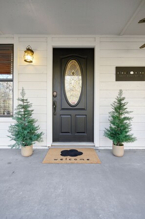 Eine Haustür mit Fußmatte, zwei Kübel-Weihnachtsbäume und einem an der Wand befestigten Schild.