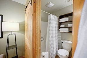 Ein Badezimmer mit Holztür, weißer Toilette, einer gestreiften Duschvorhang und einem Regal mit gefalteten Handtüchern.