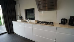 A modern kitchen with white cabinetry, a gas stove, a window with blinds, and a coffee maker. - Holiday Home in Nijkerk With Terrace (Nijkerk)