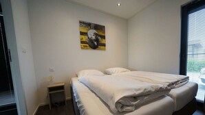 A bedroom with a bed, a nightstand, a painting, and a window with blinds. - Holiday Home in Nijkerk With Terrace (Nijkerk)