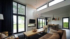 A modern living room with a sofa, a coffee table, a TV, and a dining area with chairs and a table. - Holiday Home in Nijkerk With Terrace (Nijkerk)