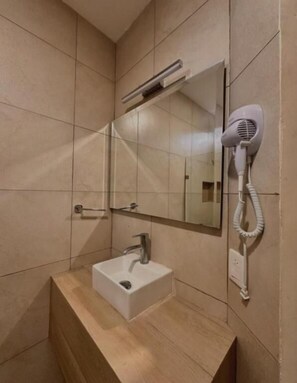 A bathroom with a sink, mirror, and hairdryer mounted on the wall.