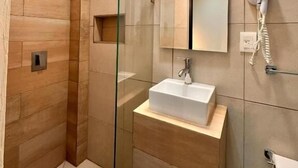 Um banheiro moderno com box de vidro, pia com espelho e secador de cabelo fixado na parede.