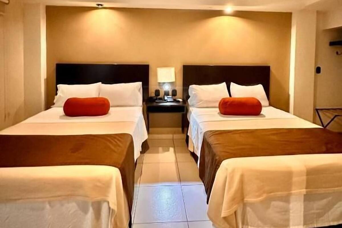 A hotel room with two beds, a nightstand, a lamp, and a chair.