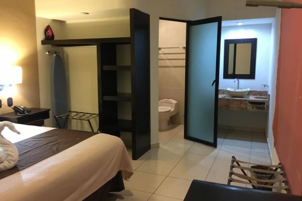 A hotel room with a bed, a desk, a chair, a bathroom with a toilet and sink, and a shower area.