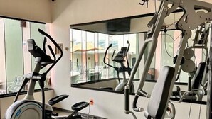 Uma academia com equipamentos de ginástica, janelas amplas e espelhos.
