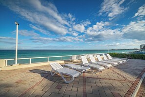 Une terrasse en bord de mer, dotée de chaises longues, d’une rambarde et offrant une vue sur l’océan.