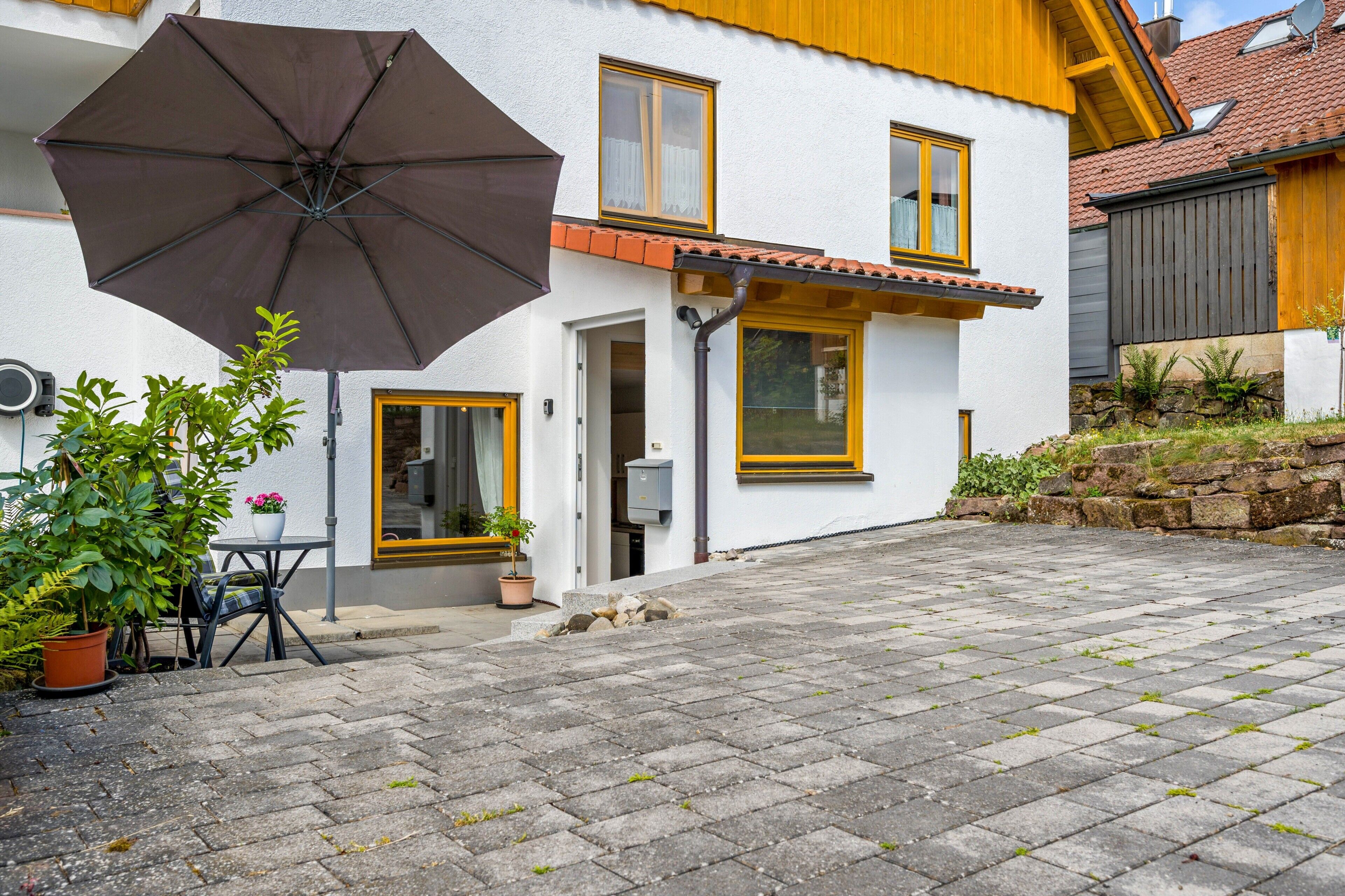 A house with a paved courtyard, a large umbrella, and potted plants.