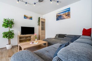 A modern living room with a sectional sofa, a flat-screen TV, a wooden coffee table, and two wall-mounted paintings.