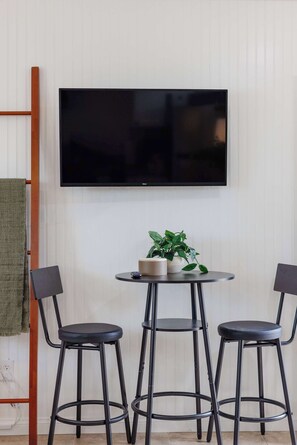 Ein modernes Zimmer mit einem flachbildfernseher an der Wand, einem runden Tisch mit zwei Stühlen und einem Blumentopf auf dem Tisch.