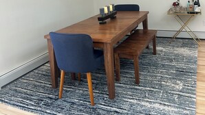 Ein Essbereich mit einem Holztisch, blauen Stühlen, einem gemusterten Teppich und gerahmten Kunstwerken an den Wänden.