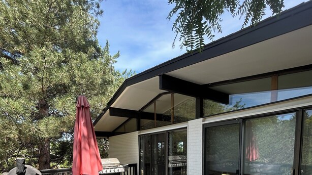 Eine Holzterrasse mit Gartenmöbeln, einem Grill und einem verglasten Lounge-Bereich.