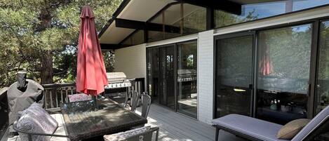 A wooden deck with outdoor furniture, a grill, and a glass-enclosed lounge area.