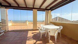 Una veranda riparata con tavolo e sedie, vista sul mare e un edificio sullo sfondo.