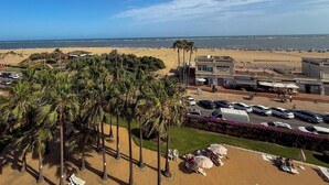 Vista sulla spiaggia con un'area di parcheggio, palme e un edificio con la scritta 'PIZZA BAR ATLANTIS'.