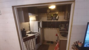 Une cuisine compacte équipée d’une cuisinière, d’un évier et de placards, qui donne sur un espace de vie avec un téléviseur.
