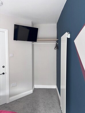 Um quarto com televisão na parede, radiador, porta e piso coberto de carpete.