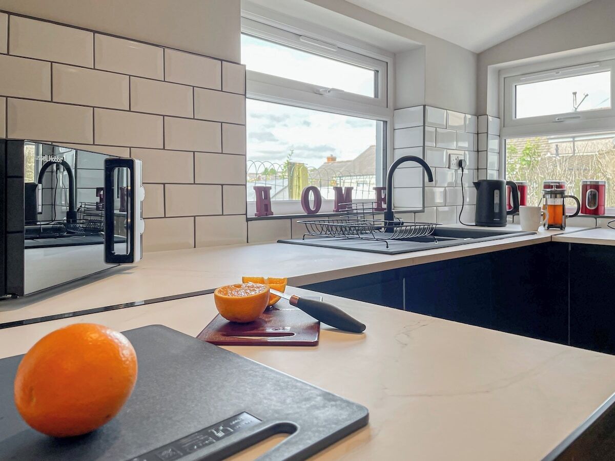 A modern kitchen with a large window, a countertop with a cutting board and orange, and a sink.