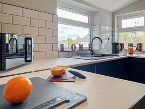 Eine moderne Küche mit einem großen Fenster, einer Arbeitsplatte mit Schneidebrett und Orangen sowie einem Spülbecken.