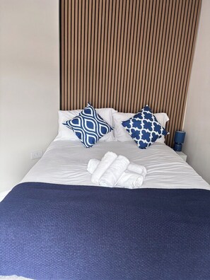 A neatly made bed with white bedding and blue patterned pillows, a blue throw blanket, and a wooden slat headboard. - Mulberry House - close to BPW and Brecons (Dowlais)