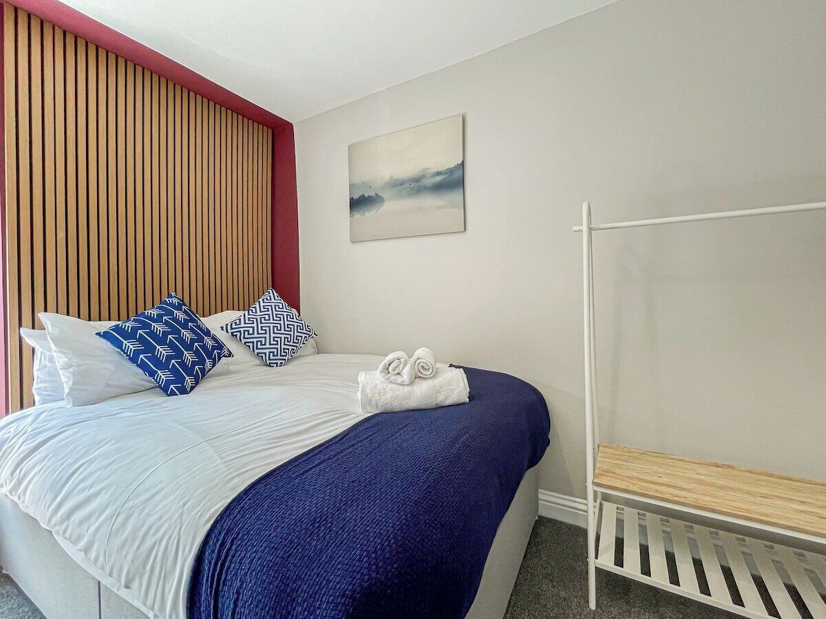 A hotel room with a bed, pillows, a blanket, a bench, and a wall-mounted picture.