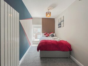 Ein schmaler Flur führt zu einem Schlafzimmer mit Bett, Fenster und Deckenventilator.