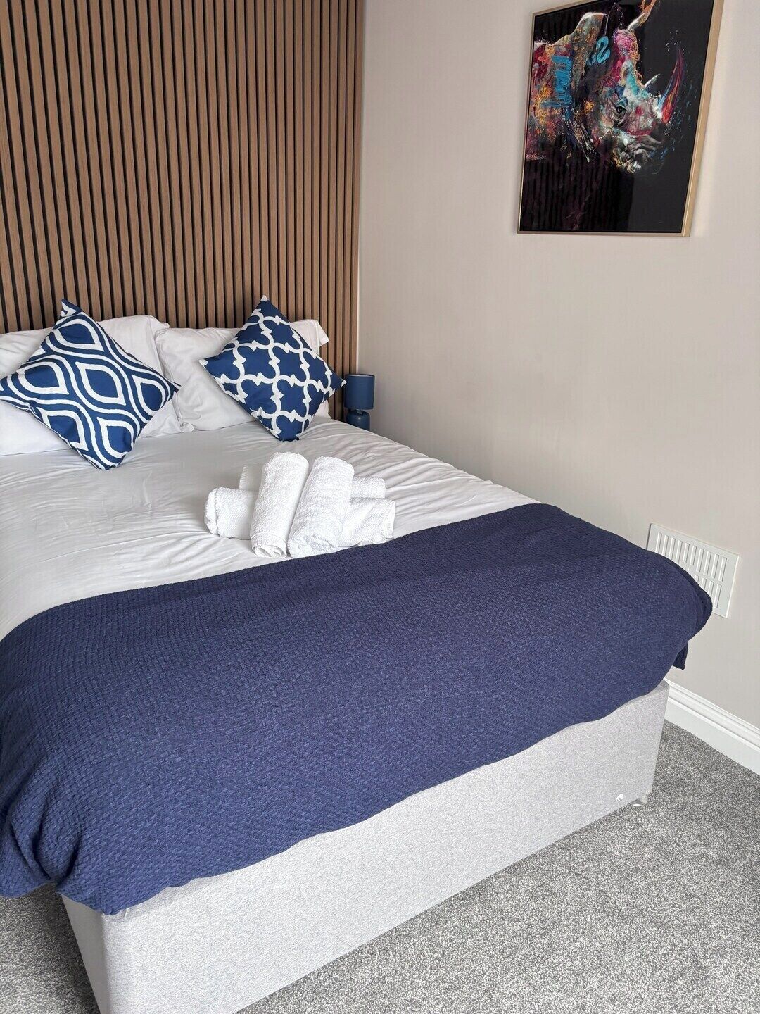 A neatly made bed with a blue and white patterned pillow, a dark blue blanket, and a white towel.