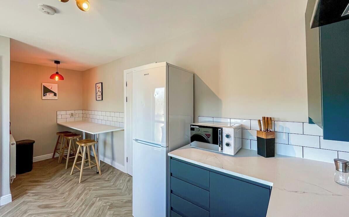 A compact kitchen with a refrigerator, microwave, and a sink. There are stools and a small table.