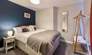 Ein Schlafzimmer mit Bett, Nachttisch, Lampe und einem Holztrockner.