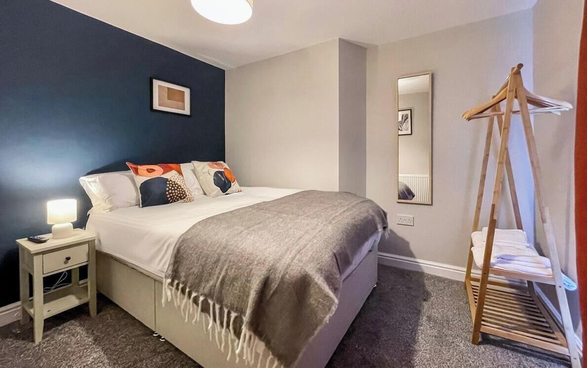 A bedroom with a bed, bedside table, lamp, and a wooden drying rack.